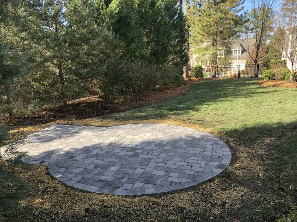 Circular gray paver patio in a sunlit wooded garden