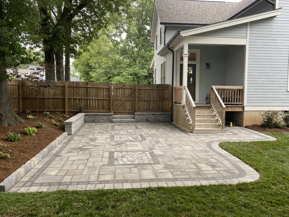 Curved gray paver patio beside back steps and a wooden fence