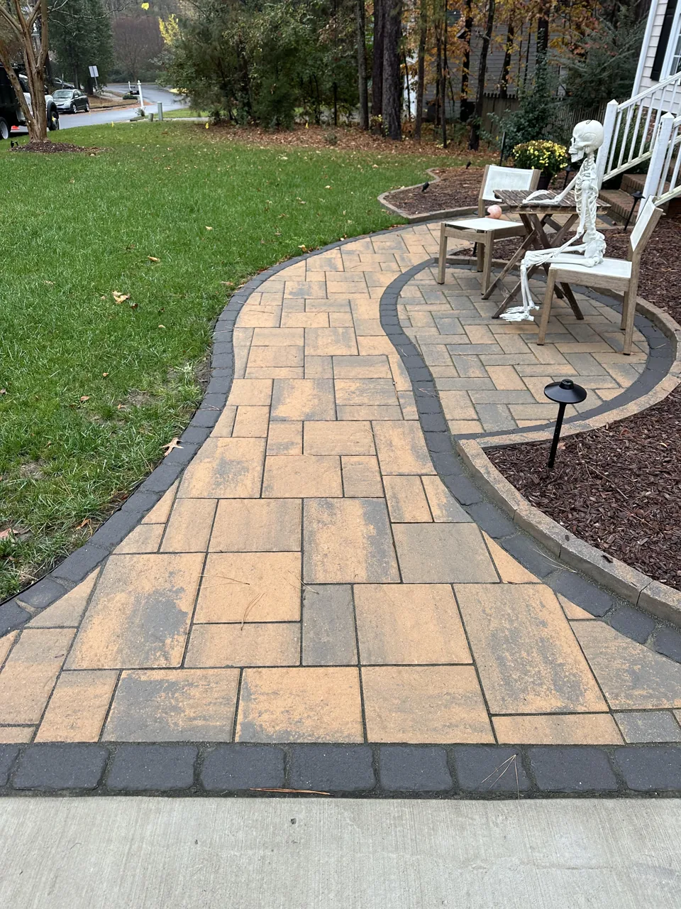 Curved multicolored paver walkway with a dark border beside green lawn