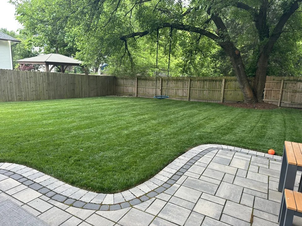 Green backyard lawn bordered by a curved gray paver patio