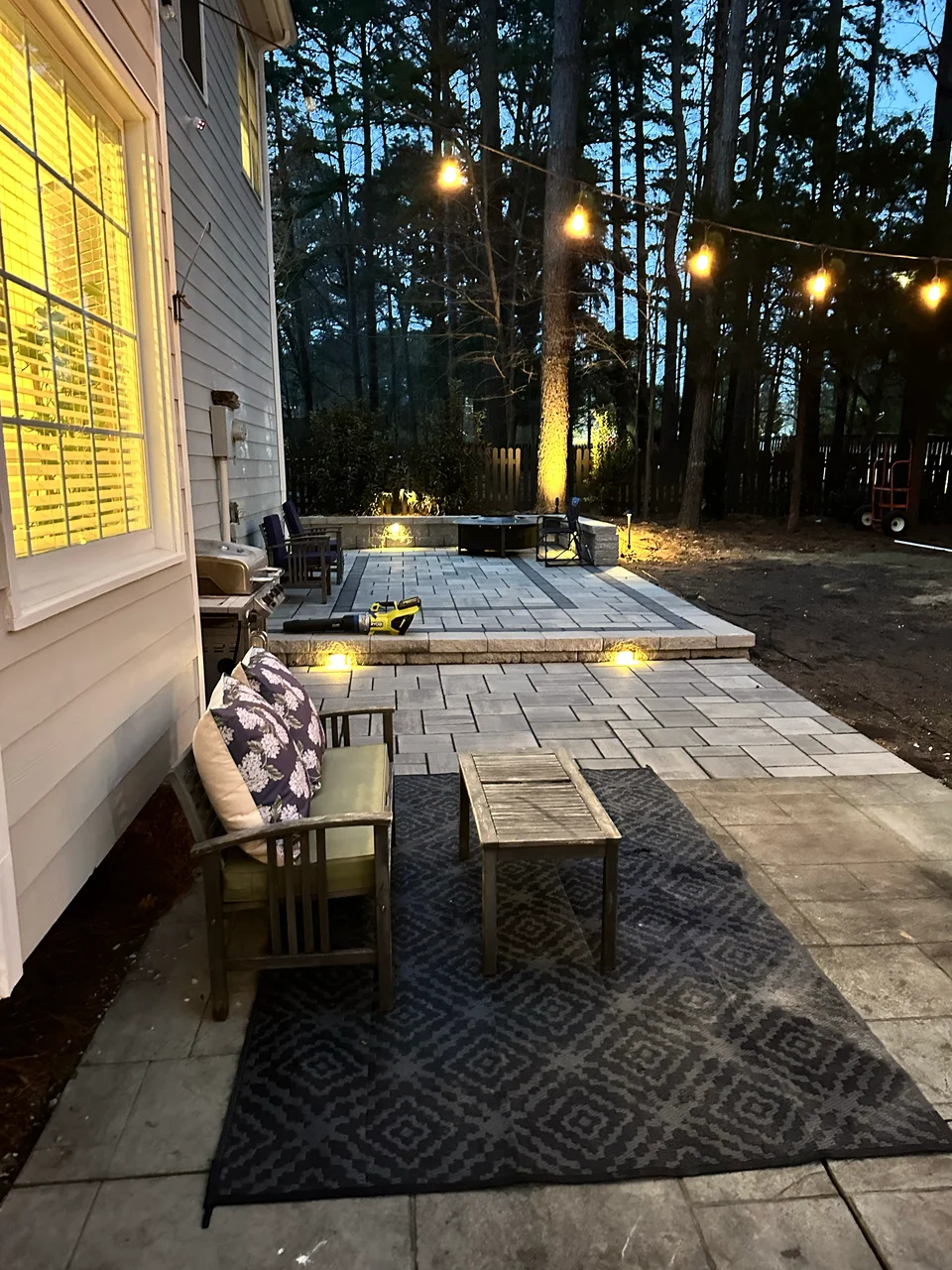 Welcoming paver patio with outdoor seating, warm string lights, and landscape lighting at dusk