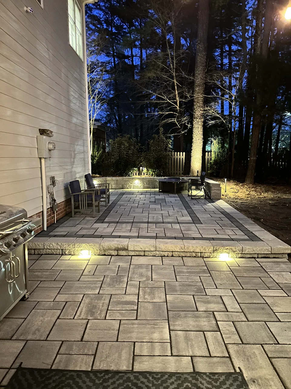 Warm lights illuminating a paver patio beside a home at dusk